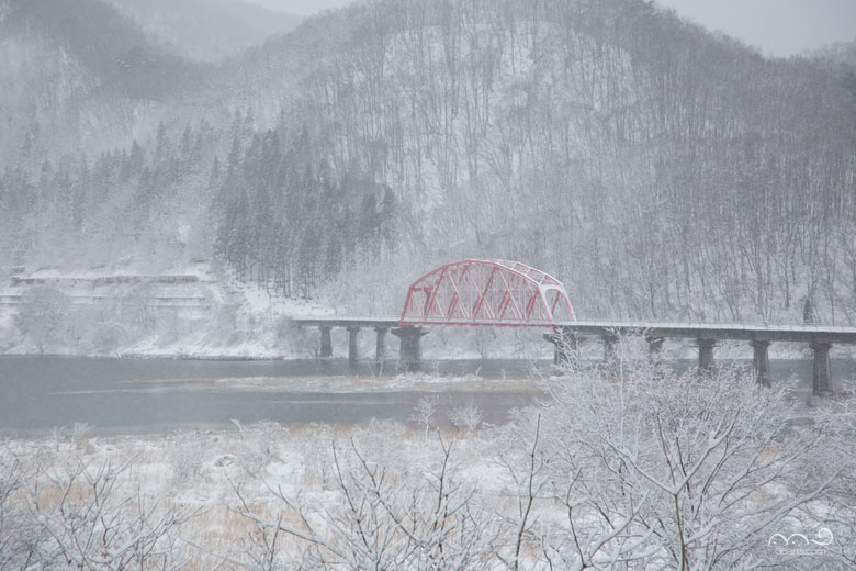 雪の降る錦秋湖と赤い鉄橋